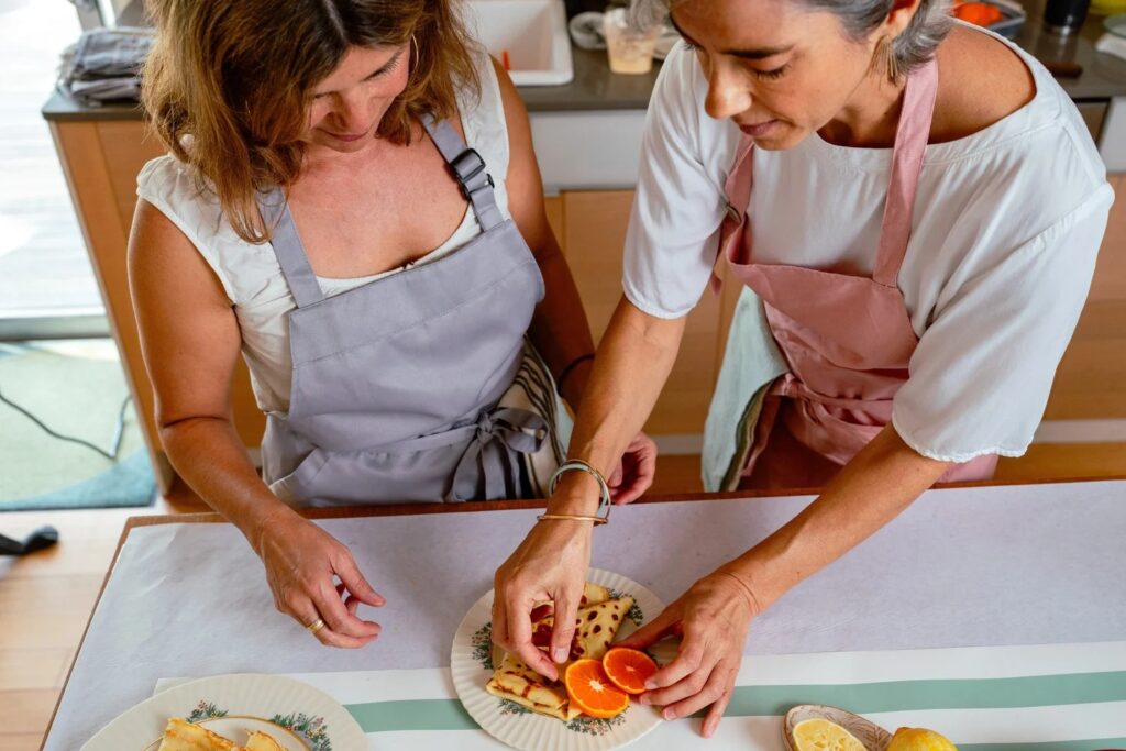 Two people plating fresh crêpes with orange slices at a The French Fold workshop in Austin