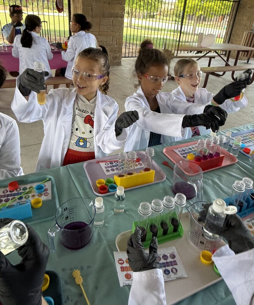 Kids in lab coats and safety goggles doing a chemistry experiment at Kids Chem Cook